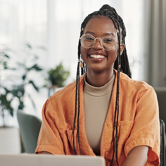 Woman with glasses smiling while working on laptop